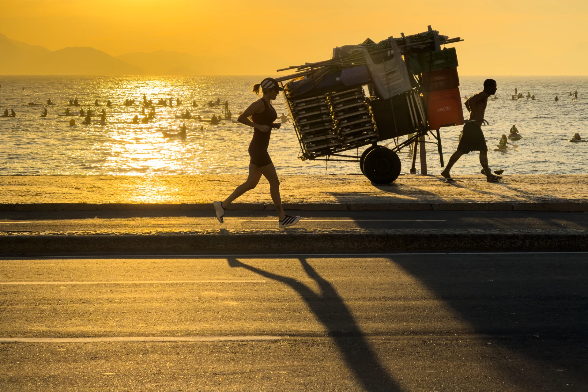 Morgenlicht an der Copacabana in Rio de Janeiro, Joggerin und Straßenhändler am Strand, goldenes Licht, lange Schatten
