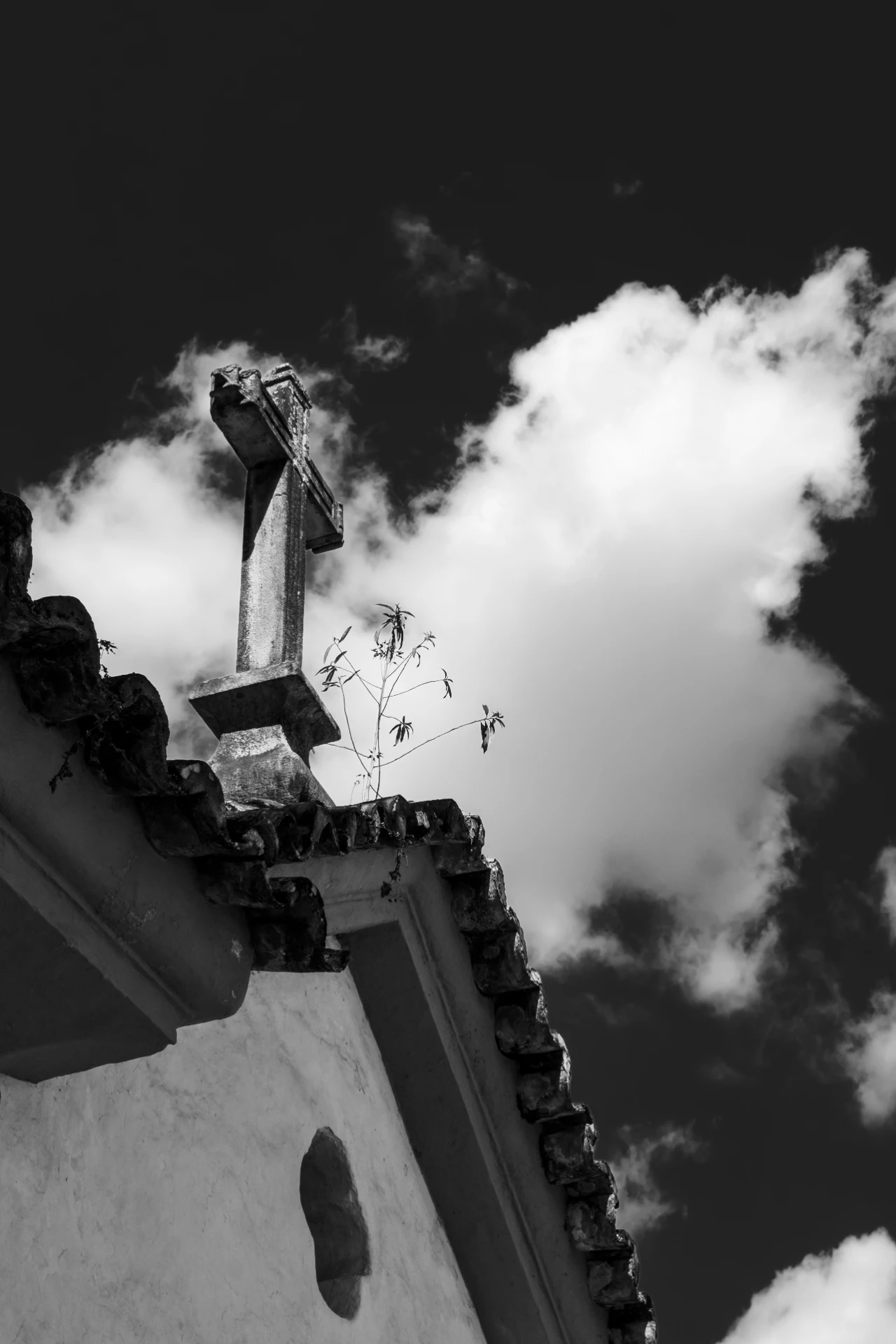 Schwarzweiß-Fotografie eines Kreuzes auf dem Dach einer Kolonialkirche in Ouro Preto, dramatischer Himmel im Hintergrund.