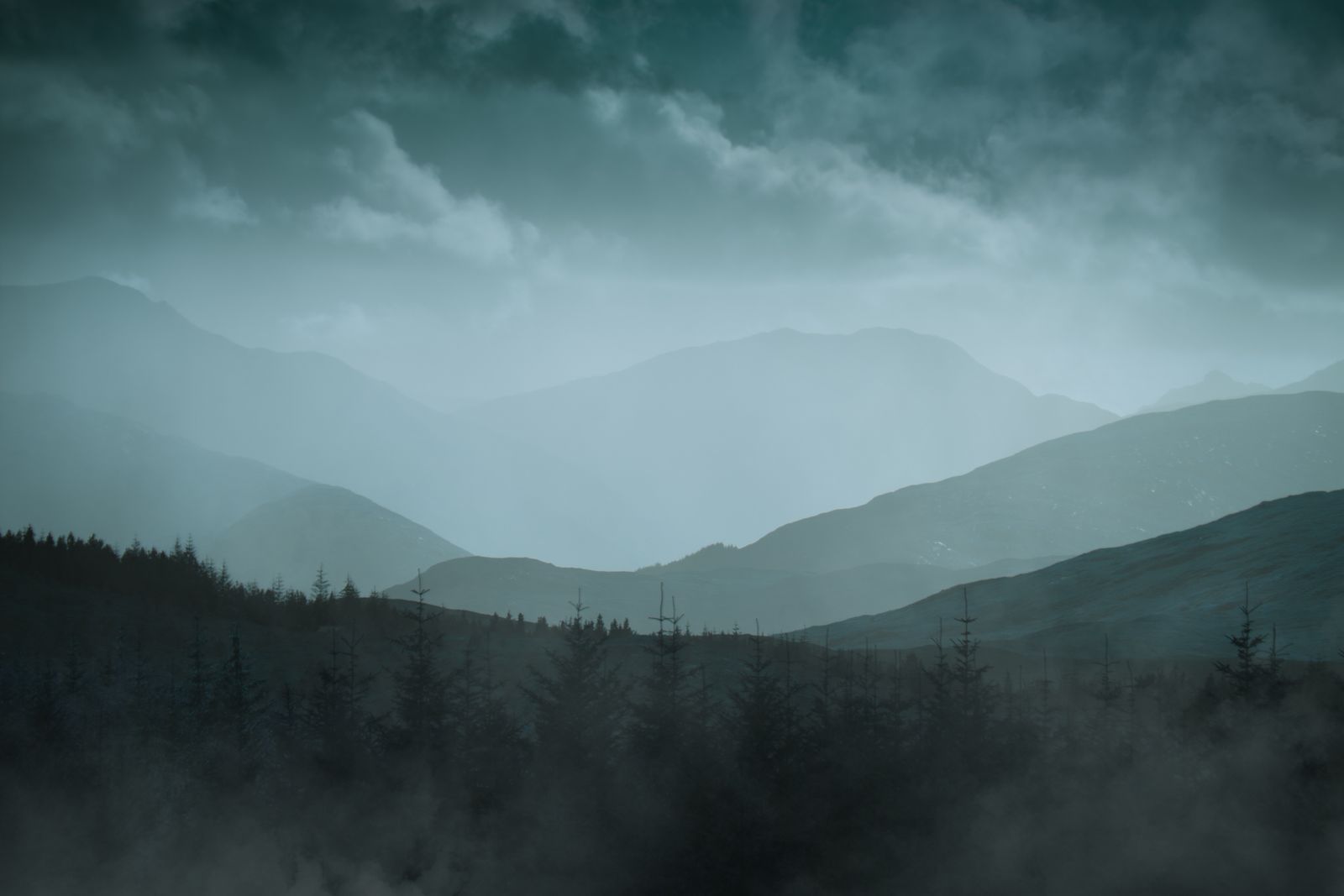 Gestaffelte Bergketten in Schottland, in dichten, blaugrünen Nebel gehüllt.