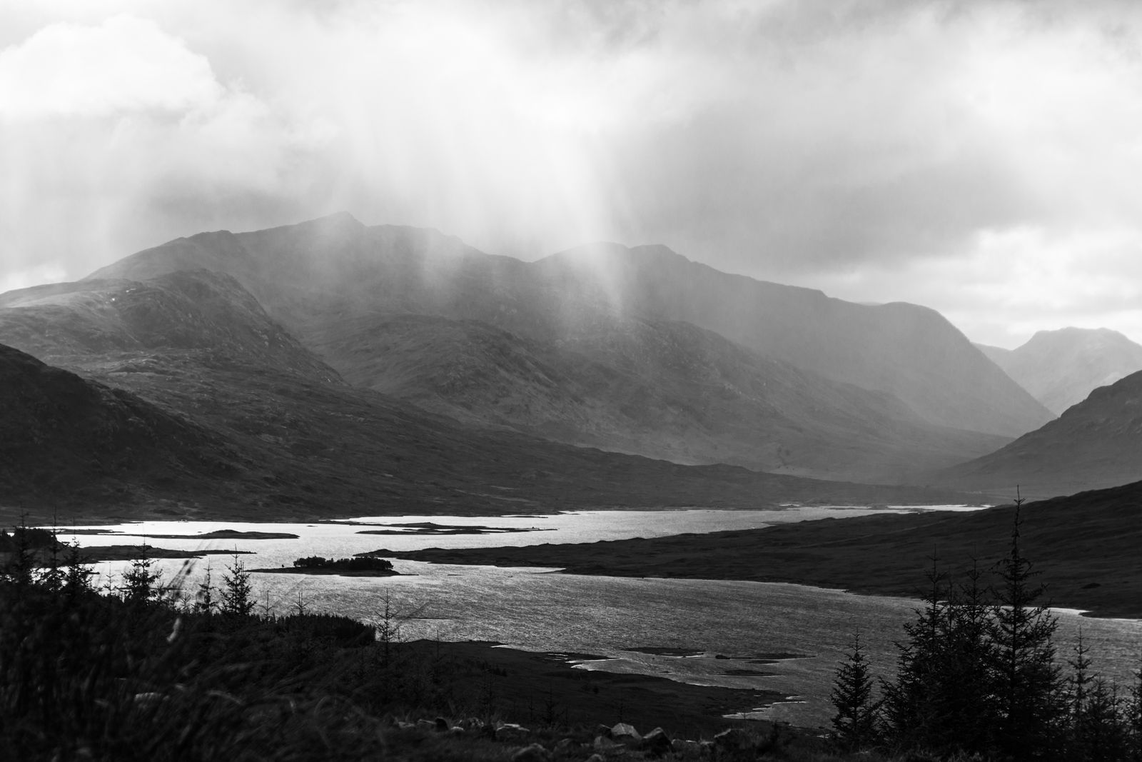 Schwarz-Weiß-Landschaft der schottischen Highlands mit See und Lichtstrahlen durch die Wolken.