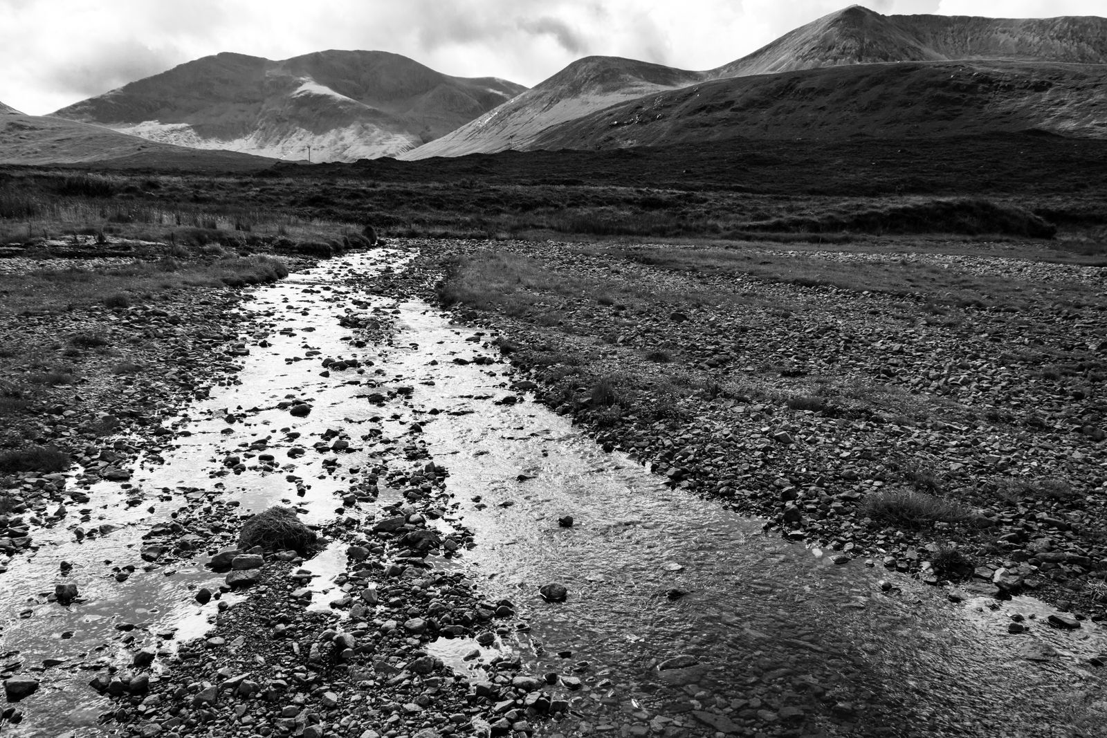 Schwarzweiß-Foto eines steinigen Flusses, der durch die Berglandschaft der Isle of Skye fließt.