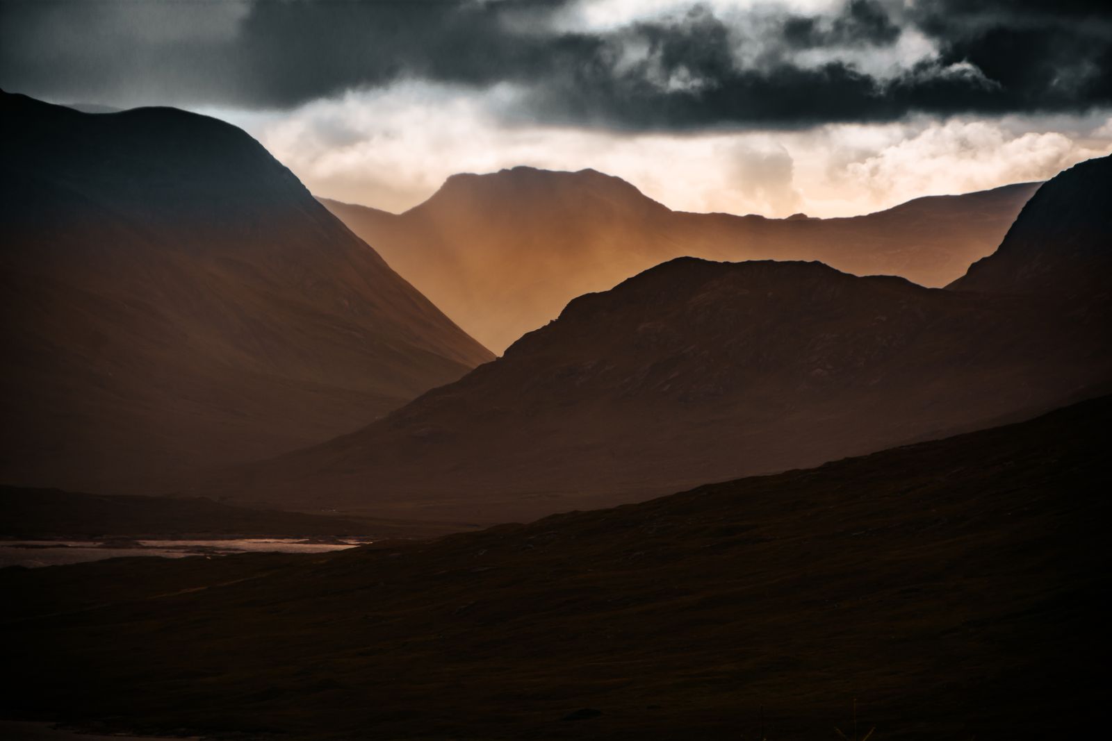 Goldenes Licht fällt durch dunkle Wolken auf eine Berglandschaft auf der schottischen Isle of Skye.