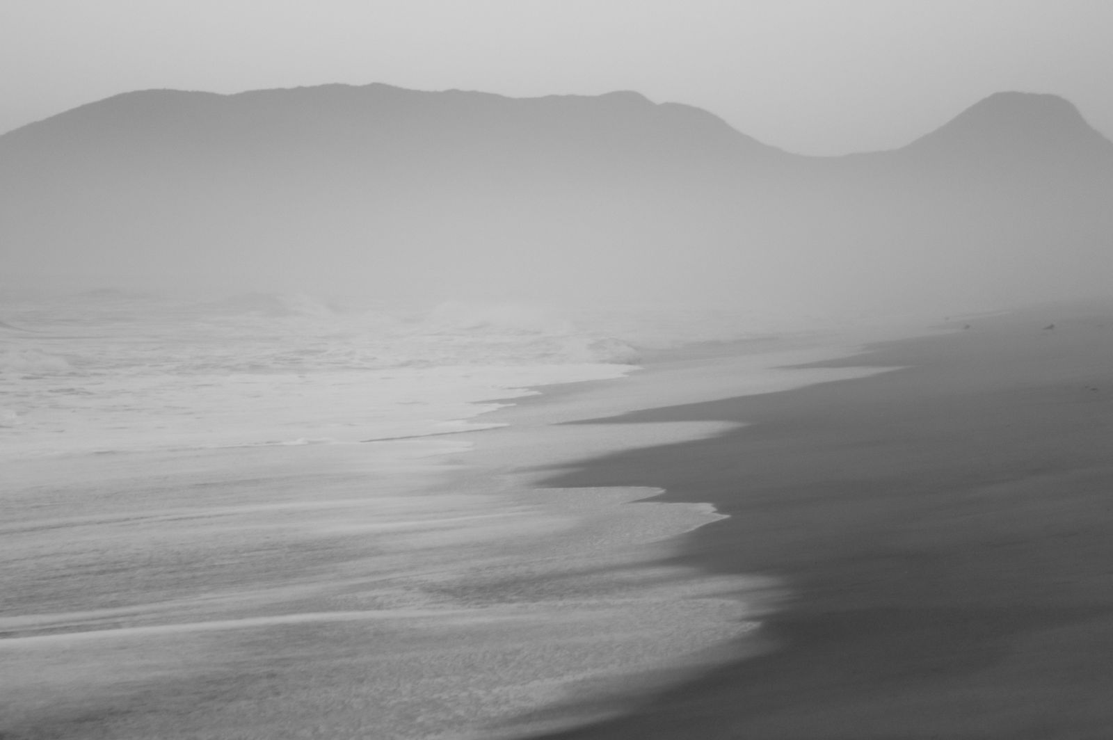 Sanfter Nebel liegt über einem weiten, menschenleeren Strand in Brasilien, das Meer verschmilzt mit dem Horizont, Licht ist gedämpft.