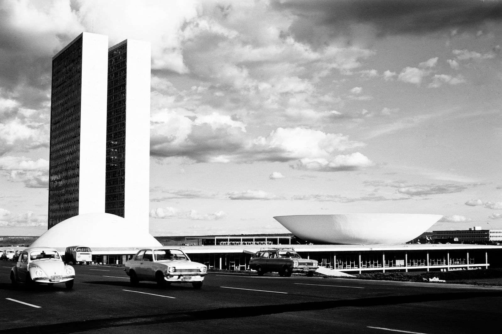 Schwarzweiß-Ansicht des Nationalkongresses in Brasília mit Autos im Vordergrund.