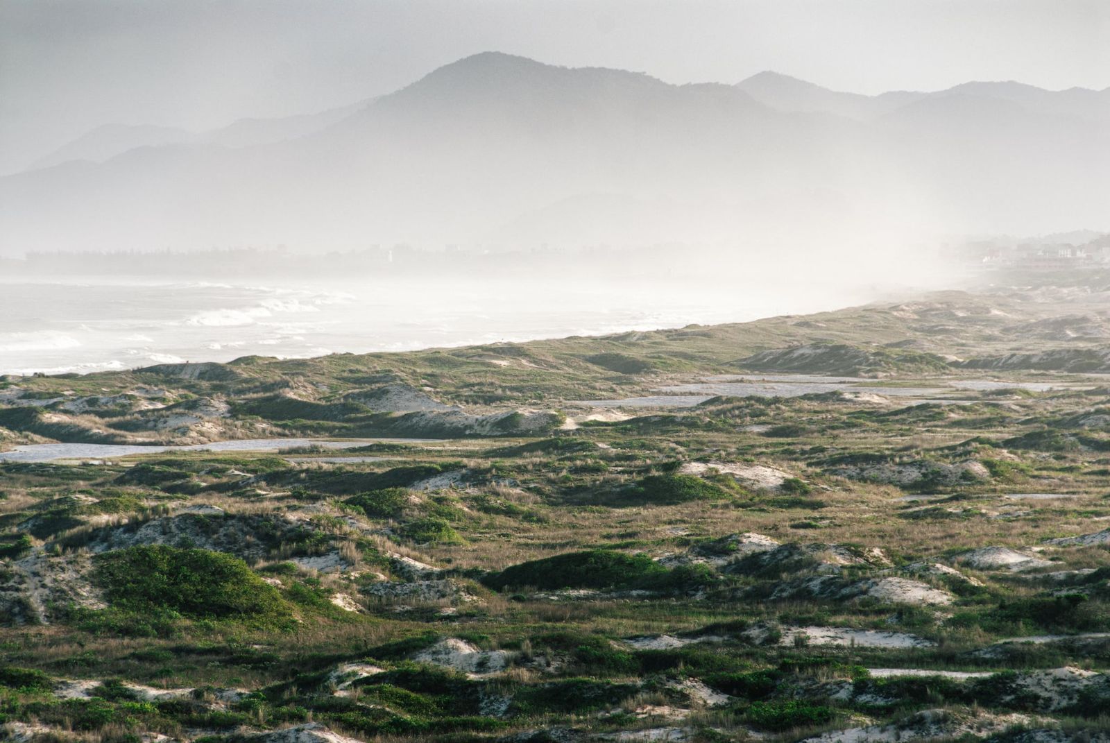 Sanftes Licht über Brasiliens Küstenlandschaft mit Felsen, Hügeln und weitem Himmel in vielfältigen Farben, minimalistisch fotografiert.