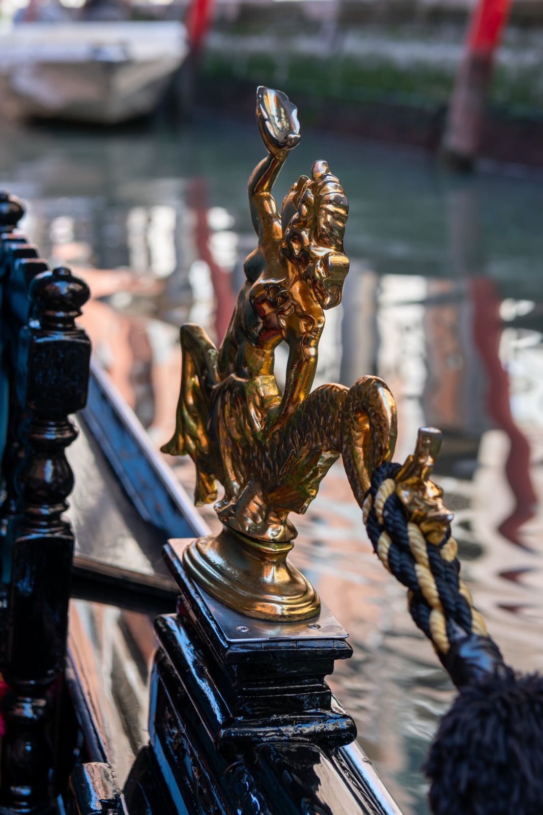 Eine kunstvoll gearbeitete Messingfigur sitzt auf einer eleganten Gondel, beleuchtet von sanftem Licht vor der Kulisse von San Marco in Venedig.