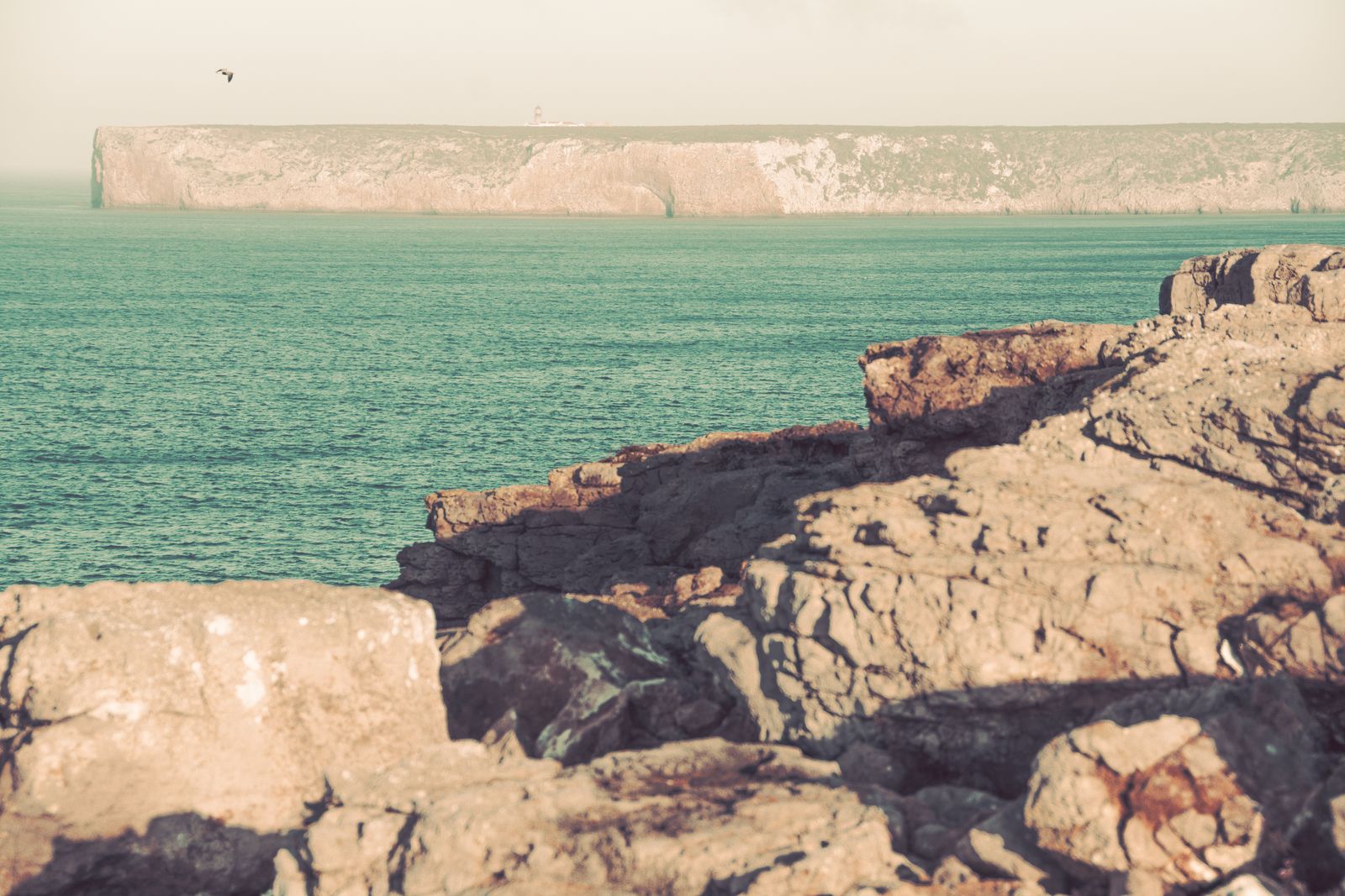Weite Felsenküste bei Sagres mit rauen Klippen, vielfältigen Naturfarben und sanftem Lichtspiel unter klarem Himmel, minimalistisch inszeniert.