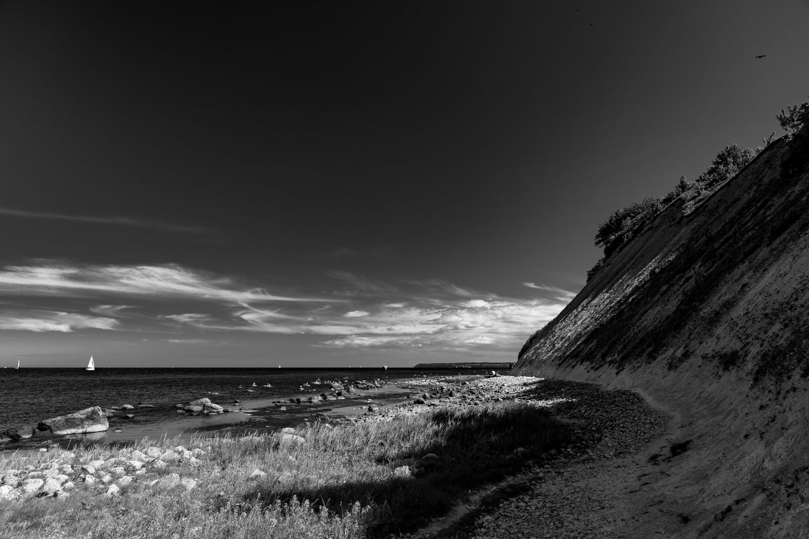 Schwarz-weiß Fotografie von Kreidefelsen bei Arkona, davor ein Segelboot auf ruhiger Ostsee unter dramatischem Wolkenhimmel