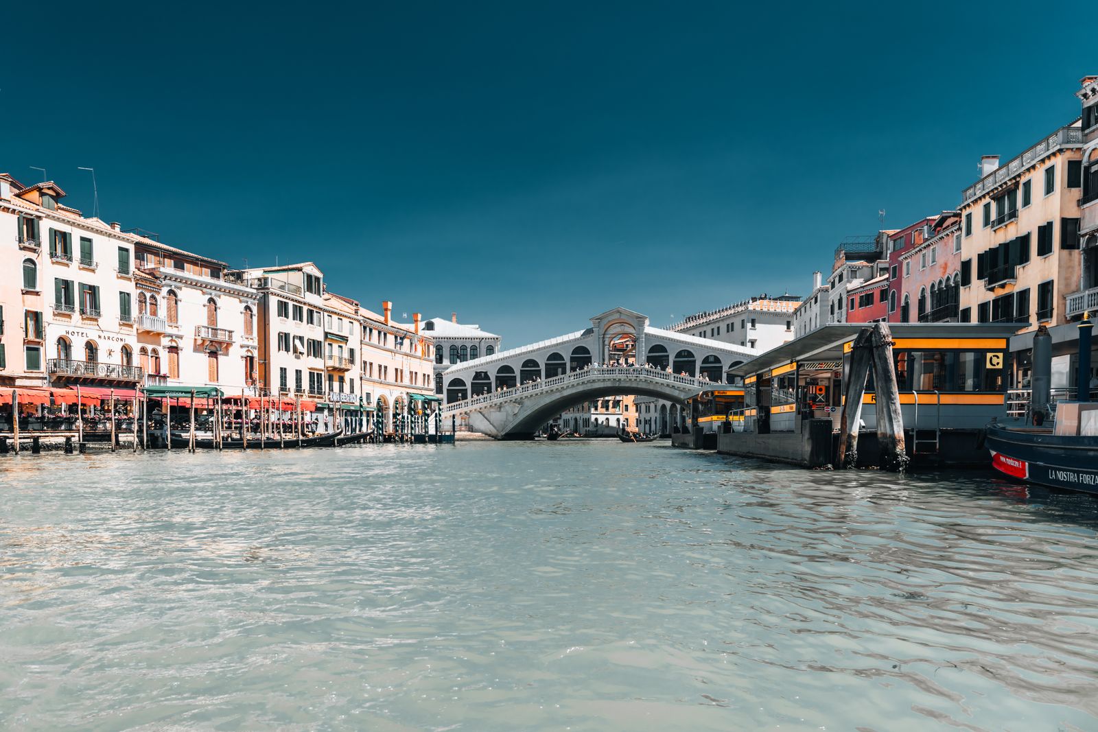 Die Rialtobrücke in Venedig, kunstvoll geschwungen, im sanften Sonnenlicht mit Spiegelung auf dem Wasser, moderne urbane Fotografie.