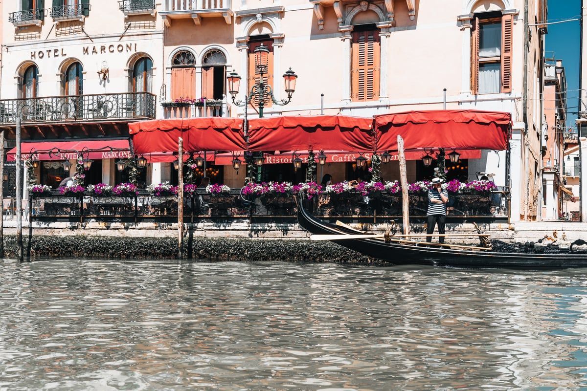 Sanfte Morgensonne beleuchtet die venezianische Uferpromenade von San Marco mit Holzstegen, ruhigem Wasser und lebendiger urbaner Atmosphäre.