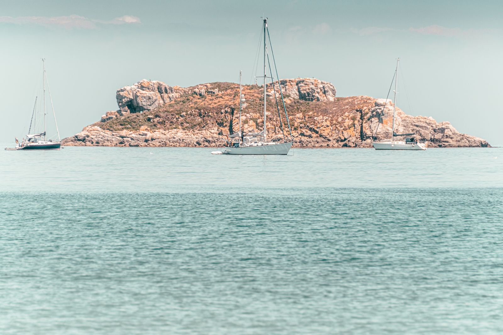 Zwei Segelboote gleiten auf ruhigem Wasser vor einer großen Felsinsel, stimmungsvolles maritimes Fotokunst-Wandbild