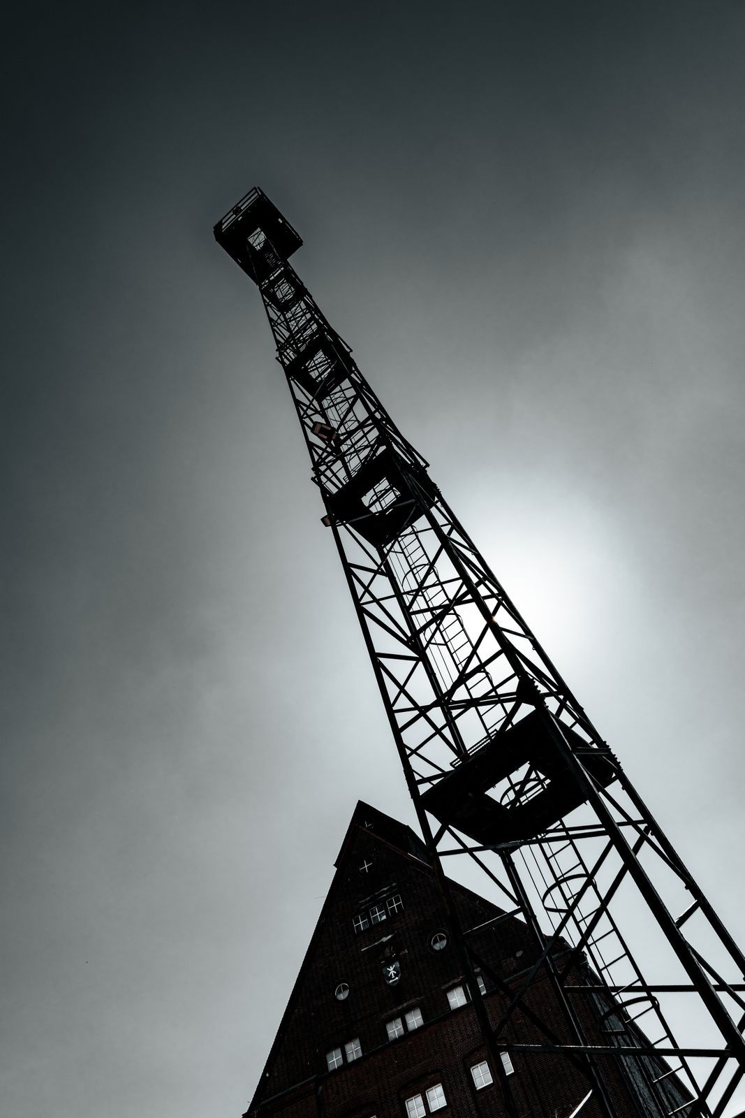 Ein alter Industriedenkmal-Turm erhebt sich als dunkle Silhouette vor einem weit geöffneten, kontrastreichen Himmel in vielfältigen Farben.