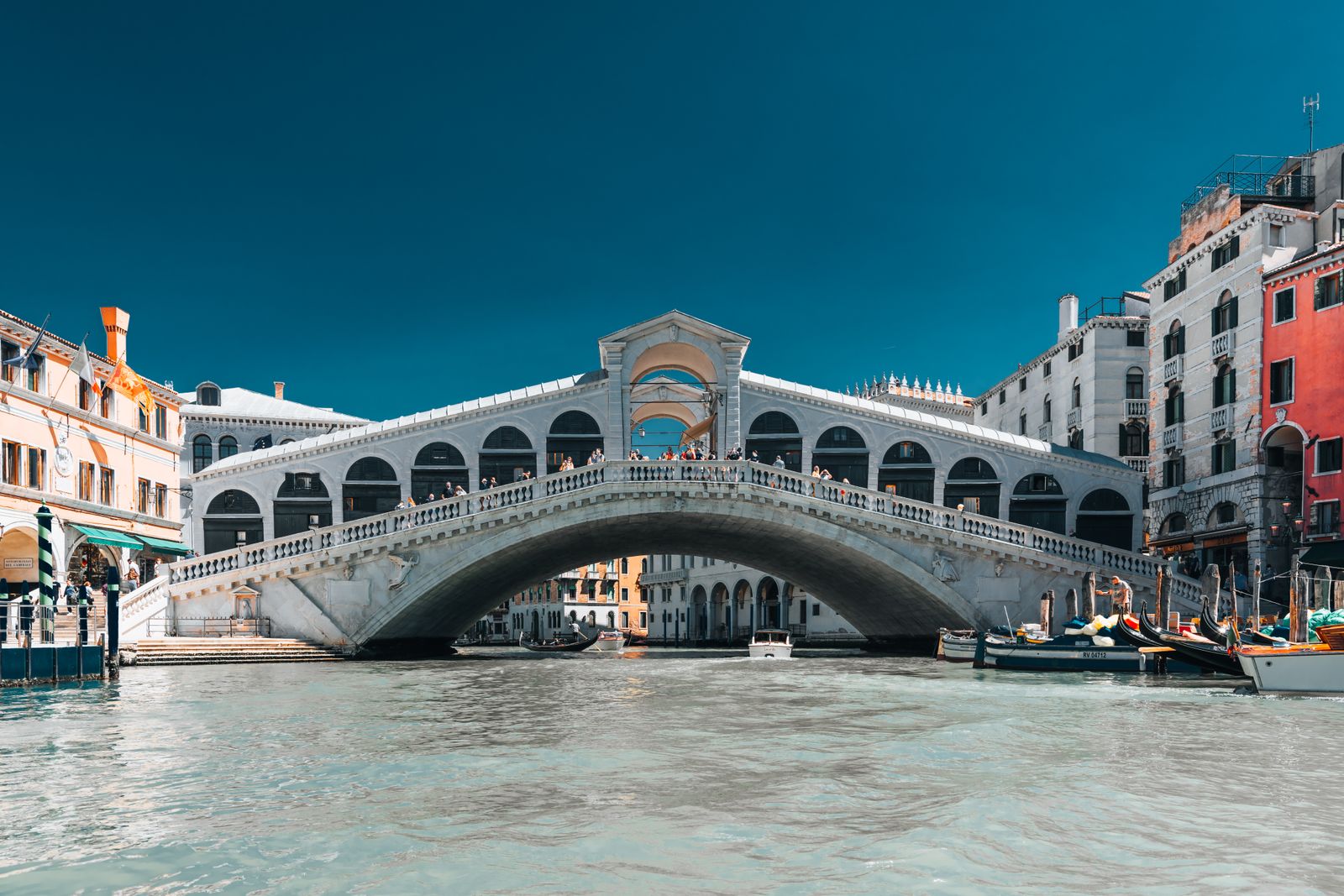 Die Rialtobrücke in Venedig bei sanftem Licht, kunstvoll geschwungen über einen breiten Kanal, umgeben von vielfältigen Farben und Wasserreflexionen.