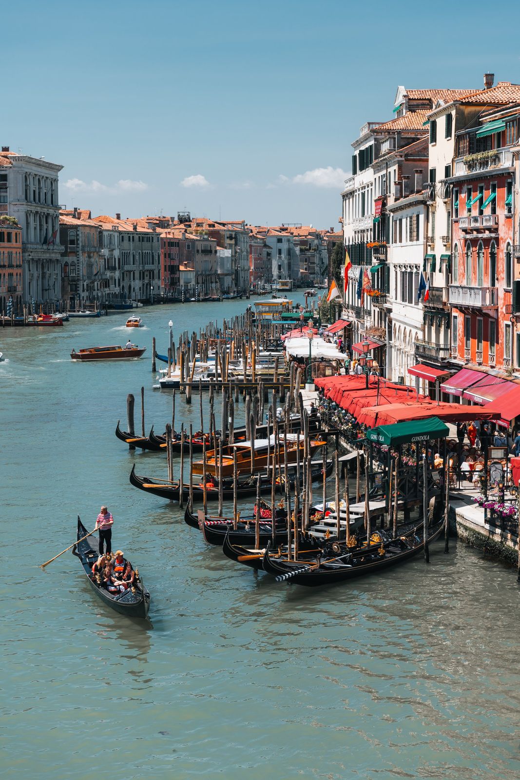 Mehrere bunte Gondeln gleiten auf dem ruhigen Canal Grande in Venedig, im Sonnenlicht vor historischen Gebäuden, lebendig eingefangen.