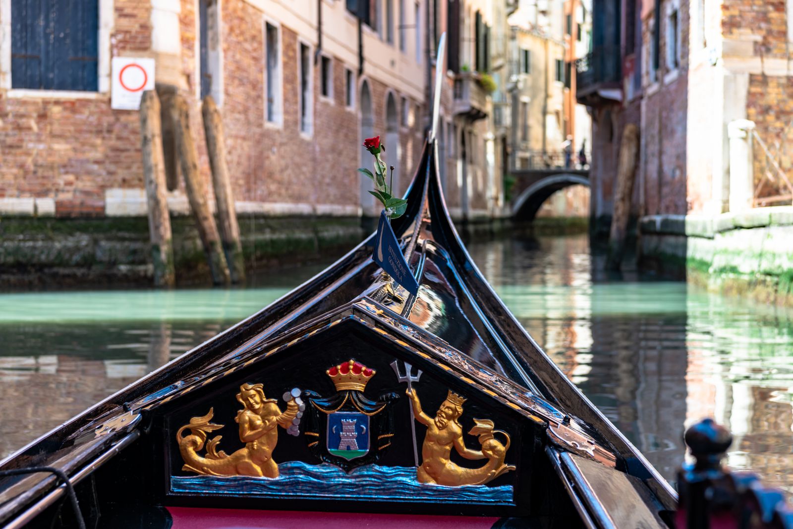 Eine Gondel gleitet bei Sonnenlicht über das Wasser vor San Marco, im Hintergrund historische Gebäude und lebendige Farben.