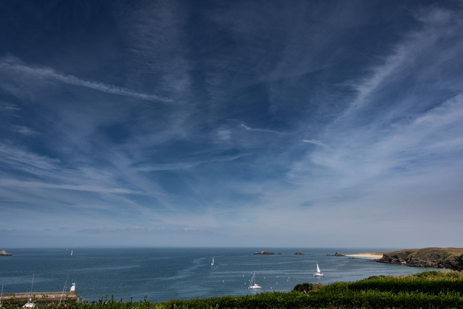 Sanfte Küstenlandschaft der Bretagne mit rauen Felsen, geschwungenen Buchten und weitem Meer unter leicht bewölktem Himmel.