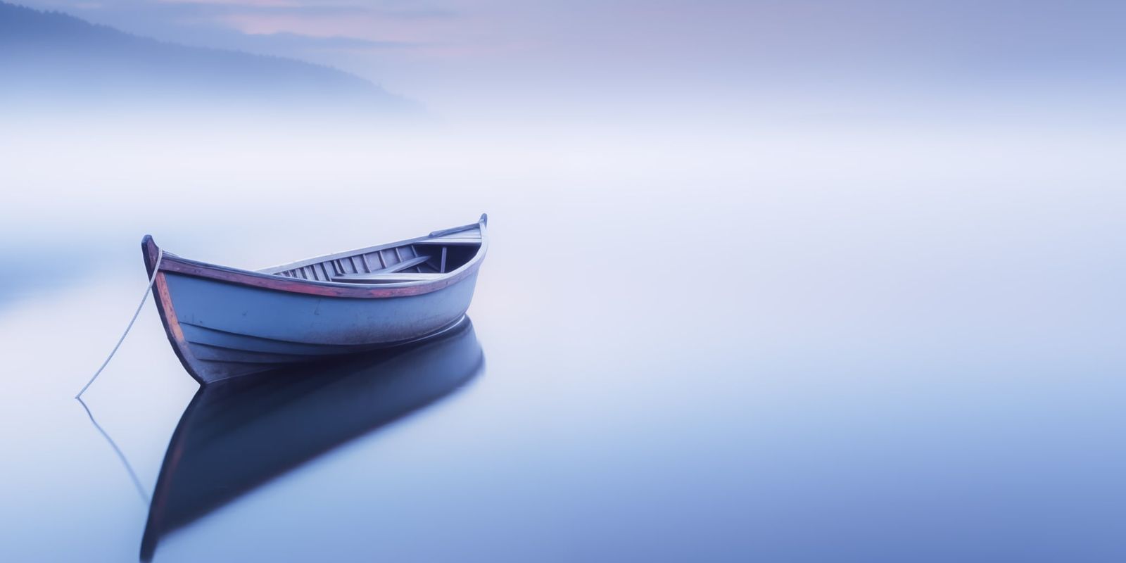 Ein einzelnes Boot liegt ruhig im dichten Morgennebel auf dem Wasser, die Szene wirkt minimalistisch und friedlich.