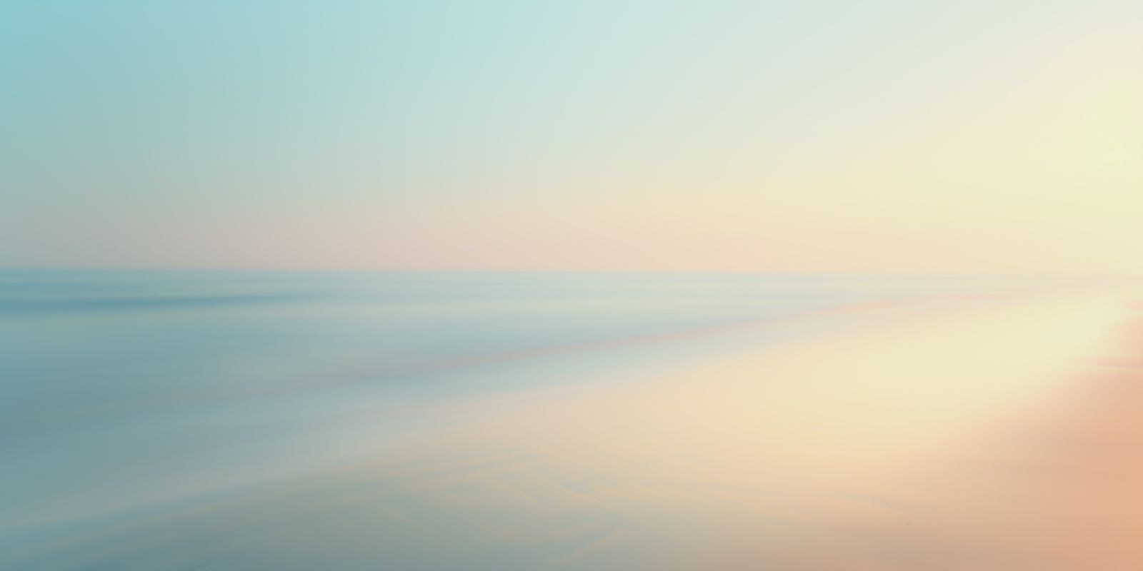 Minimalistische Fotografie einer sanften Küstenlinie im Morgenlicht mit Ozean, Sand und Himmel in ruhigen, vielfältigen Farben.