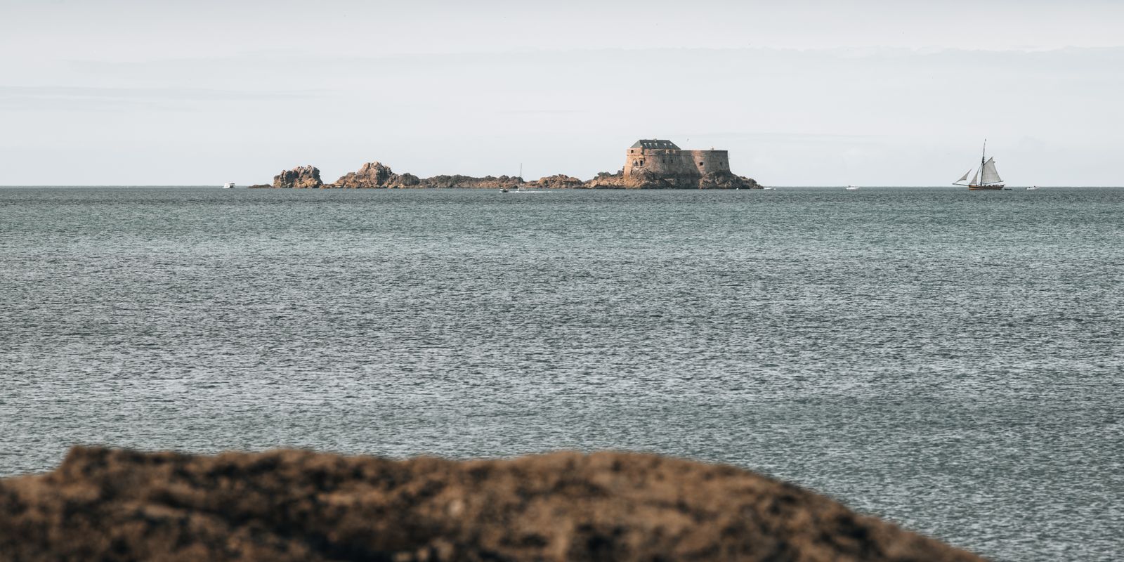 Das minimalistische Panorama zeigt das Fort National auf einer kleinen Insel vor Saint-Malo in der Bretagne, umgeben von ruhigem Meer und weitem Himmel.