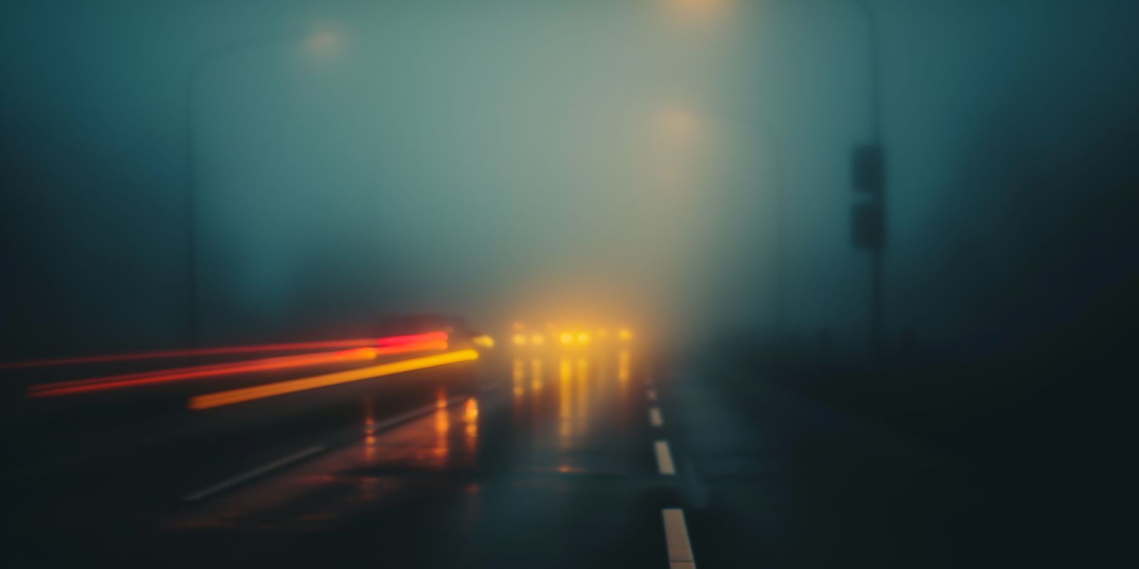 Eine nächtliche Straße zieht sich als Lichtstreif durch dichten Nebel, umgeben von Dunkelheit und geheimnisvoller Atmosphäre.
