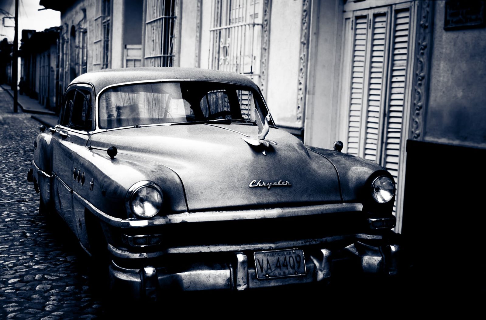 Ein farbenprächtiger, restaurierter Chrysler Oldtimer steht auf einer sonnigen Straße in Kuba, umgeben von kolonialen Gebäuden.