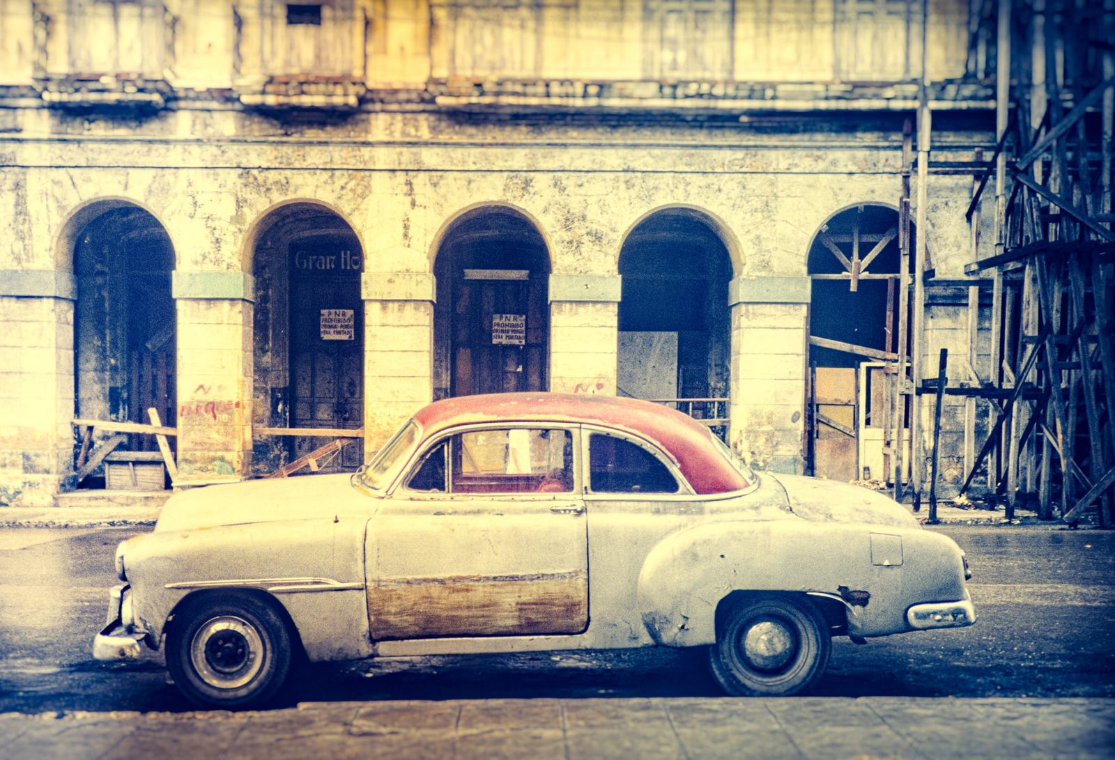 Bunter amerikanischer Oldtimer steht vor einer farbenfrohen, kolonialen Hausfassade in Havanna, Kuba, im Vintage-Stil fotografiert.