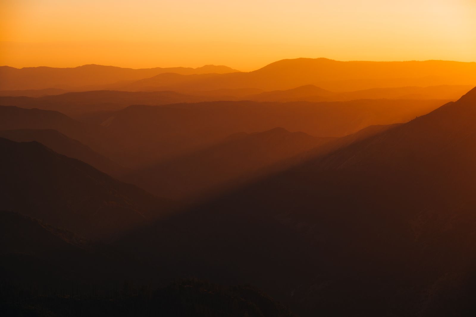 Mehrere sanfte Bergsilhouetten im warmen Abendlicht, minimalistisch fotografiert, mit ruhigen Licht- und Schattenverläufen