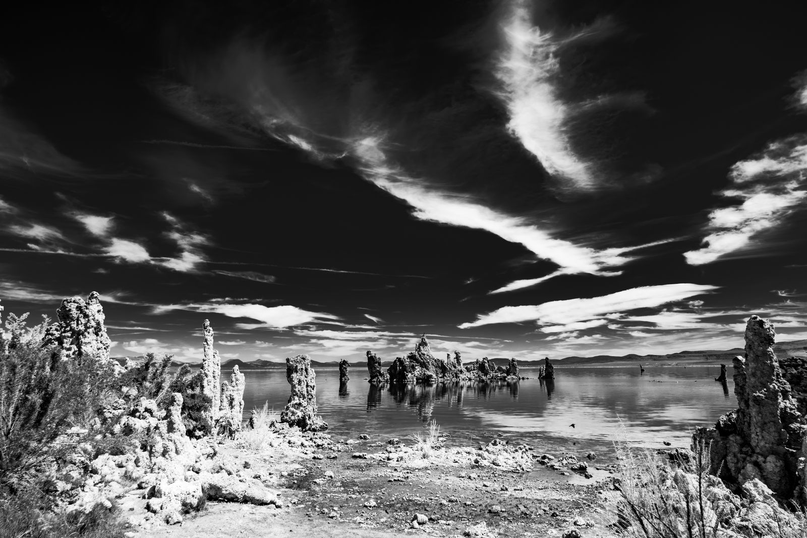 Schwarzweiß-Fotografie der Mono Lake Kalktuff-Formationen, dramatisch beleuchtet, ruhige Wasseroberfläche und klarer Himmel im Hintergrund