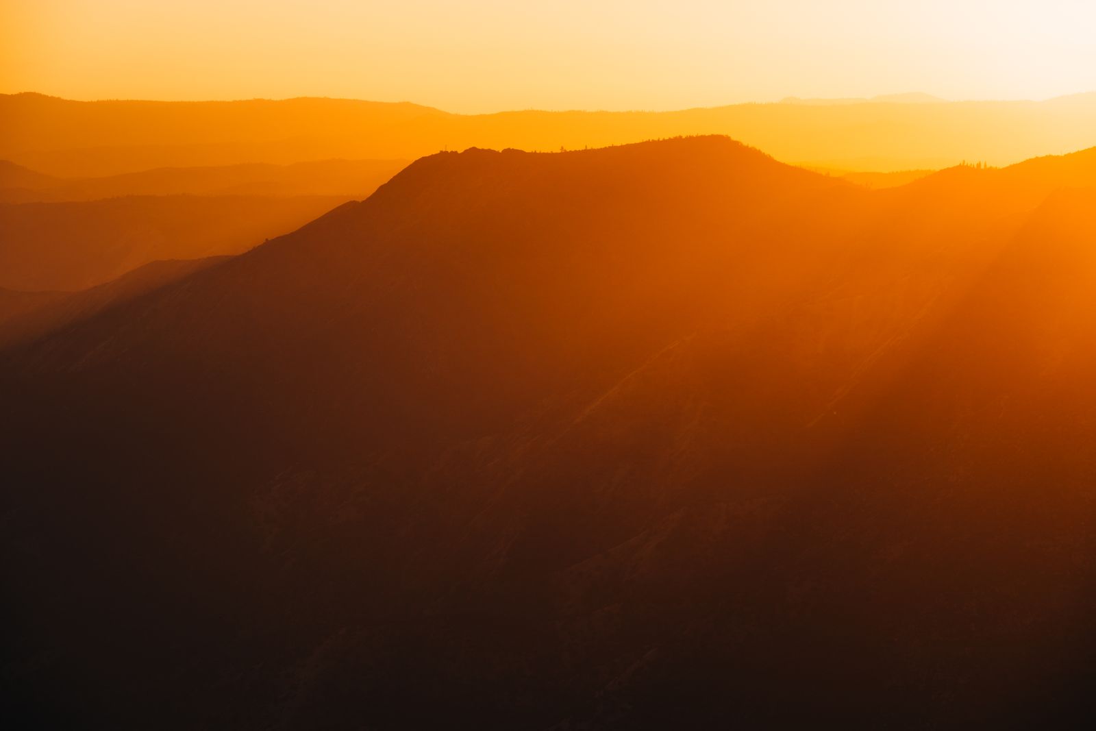 Minimalistisches Wandbild zeigt einen warmen Sonnenuntergang hinter ruhigen Bergsilhouetten, sanfte Farbübergänge am Himmel, stimmungsvolle Natur.