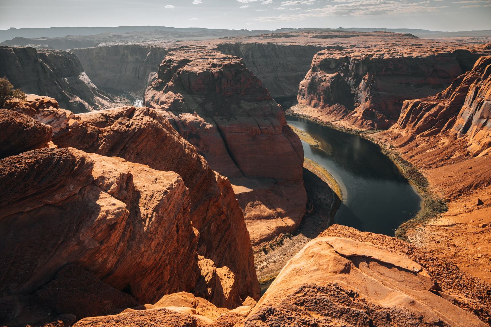 Weit geschwungene Flussbiegung des Horseshoe Bend in Arizona, eingerahmt von rotgoldener, karger Landschaft unter klarem Himmel.