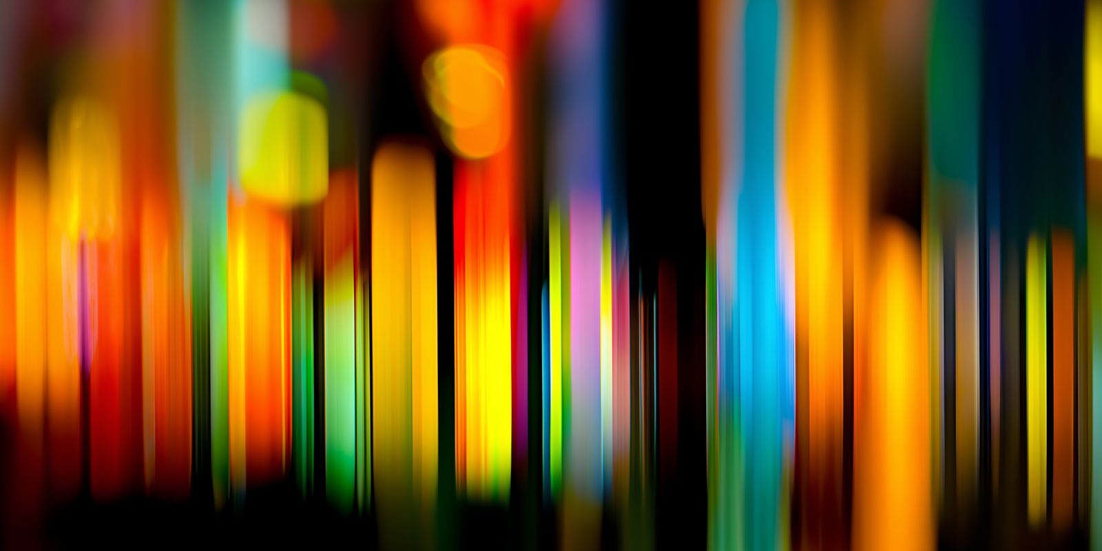 Leuchtende, farbintensive Lichtstreifen verlaufen abstrakt und dynamisch quer über das Panorama-Bild auf dunklem Hintergrund.