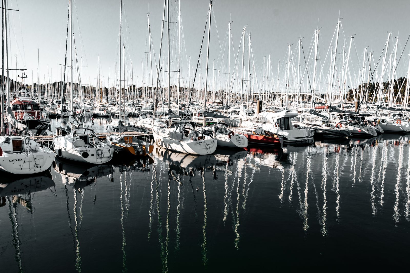 Mehrere Segelboote liegen ruhig nebeneinander im Hafenbecken, das Wasser spiegelt die Boote und die sanfte Lichtstimmung wider.