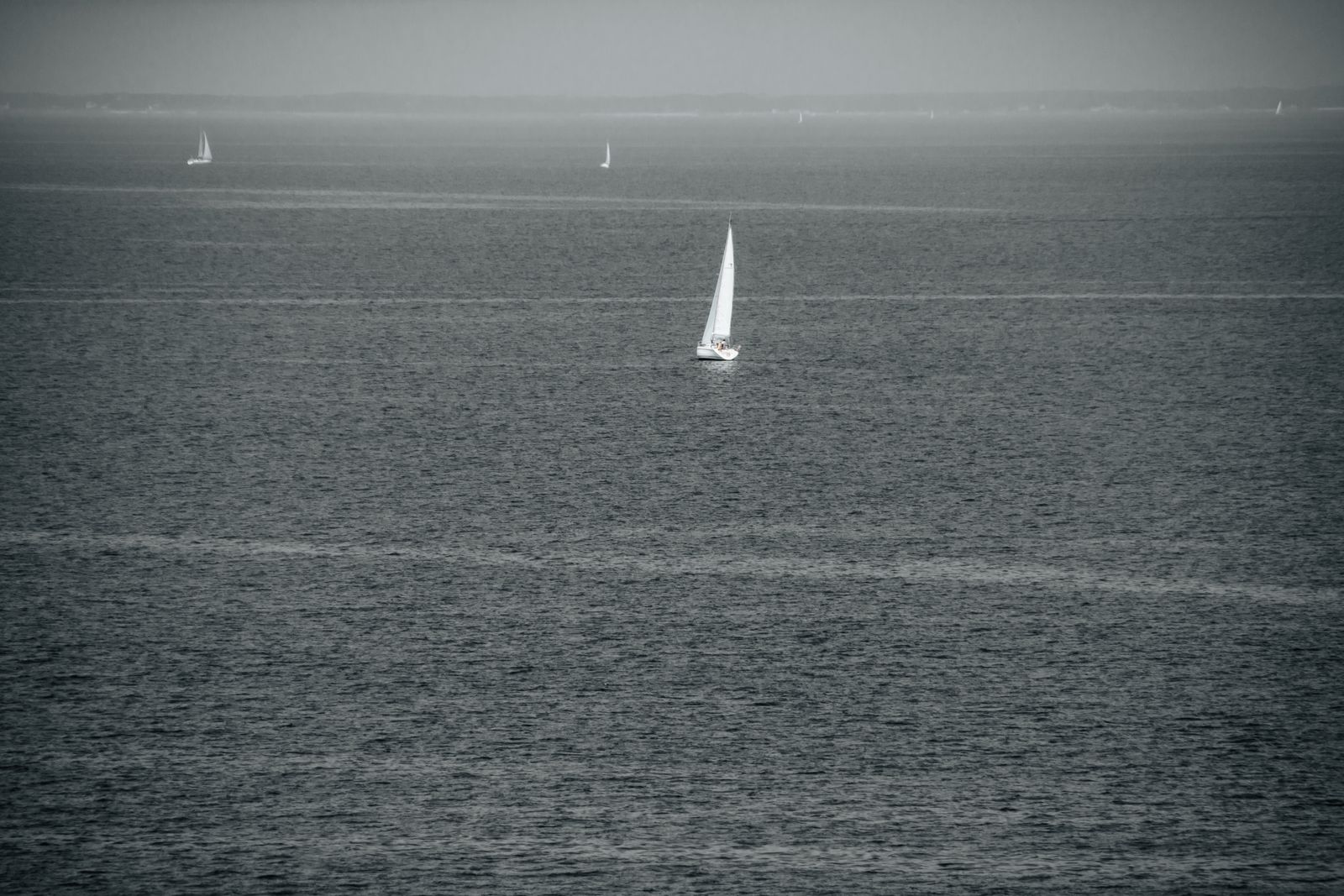 Einzelnes Segelboot gleitet ruhig über die glatte Ostsee, minimalistische Fotokunst mit sanften Farben und entspannter, maritimer Stimmung.