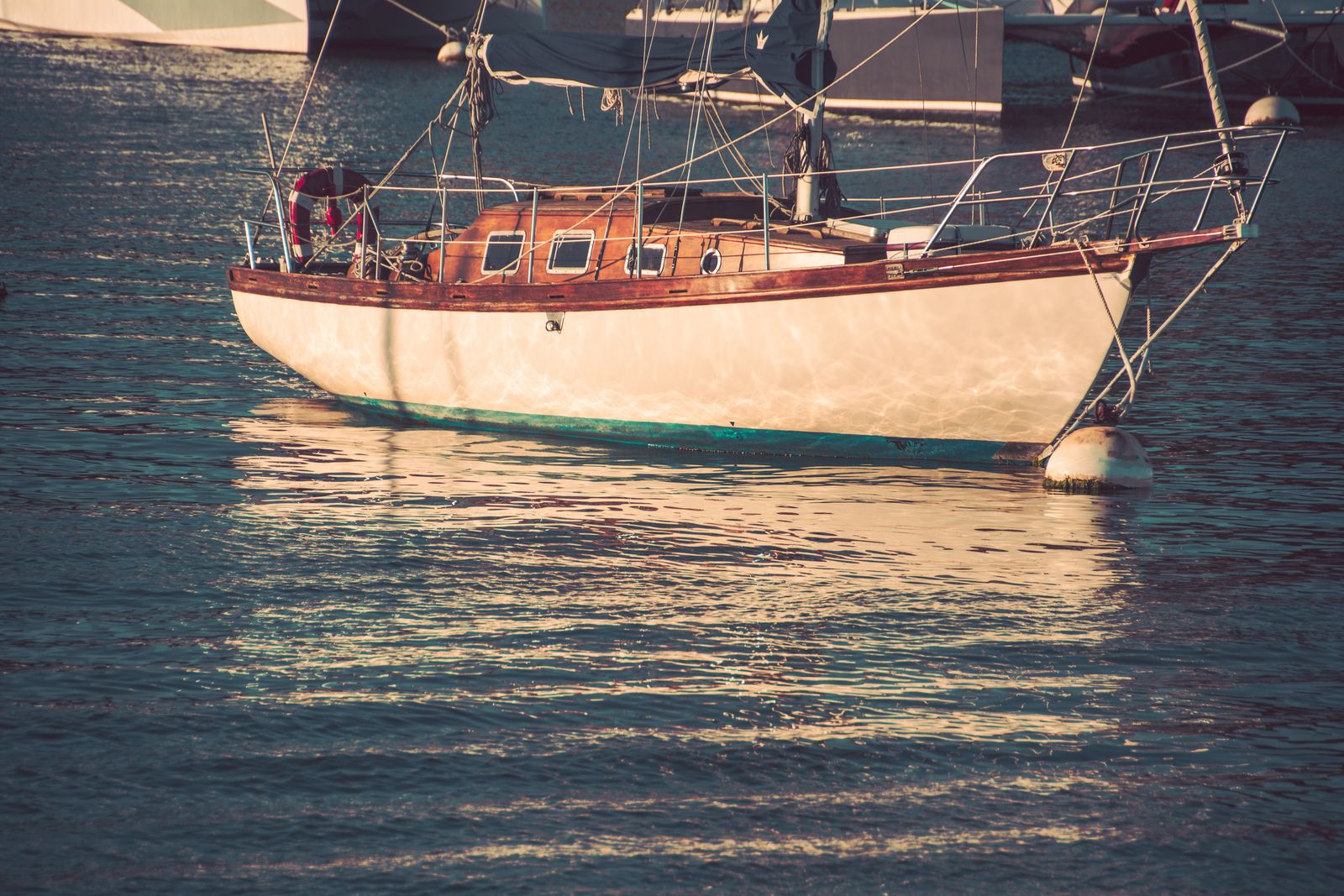 Ein Segelboot gleitet bei warmem Abendlicht ruhig über stilles Wasser, umgeben von sanften Farben und maritimer Atmosphäre.