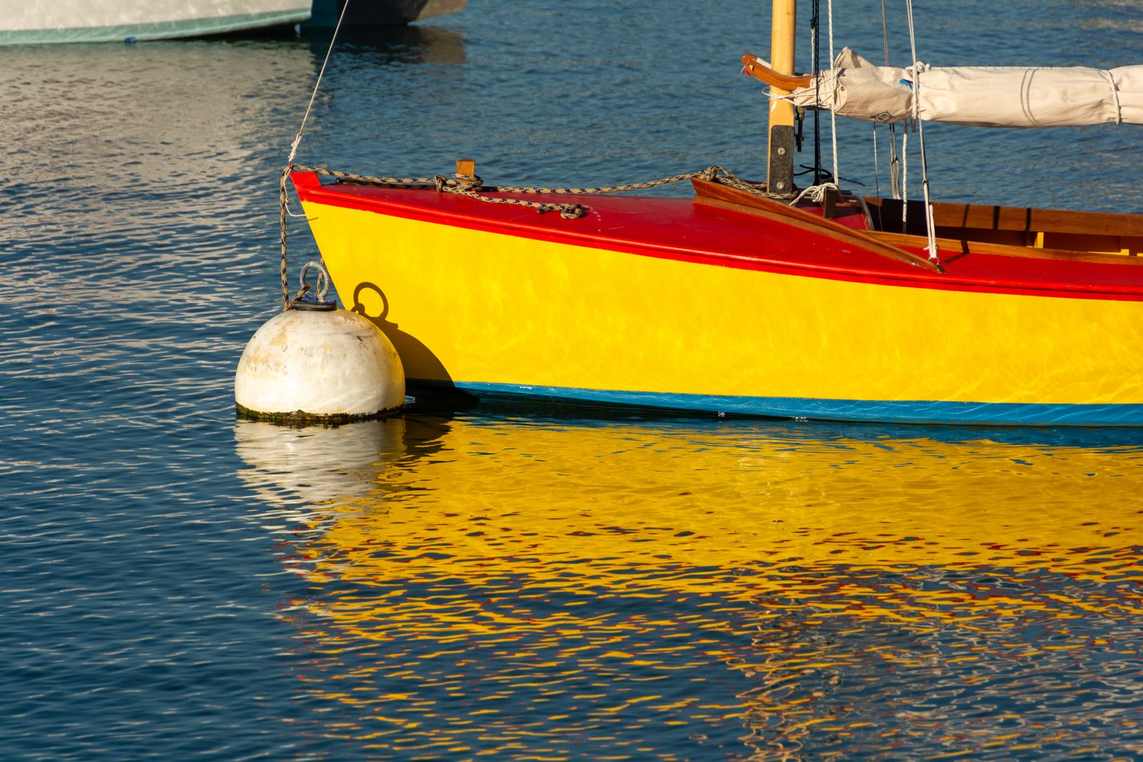 Ein buntes Boot liegt ruhig im klaren Hafenwasser, umgeben von sanften Reflexionen und maritimer Atmosphäre.