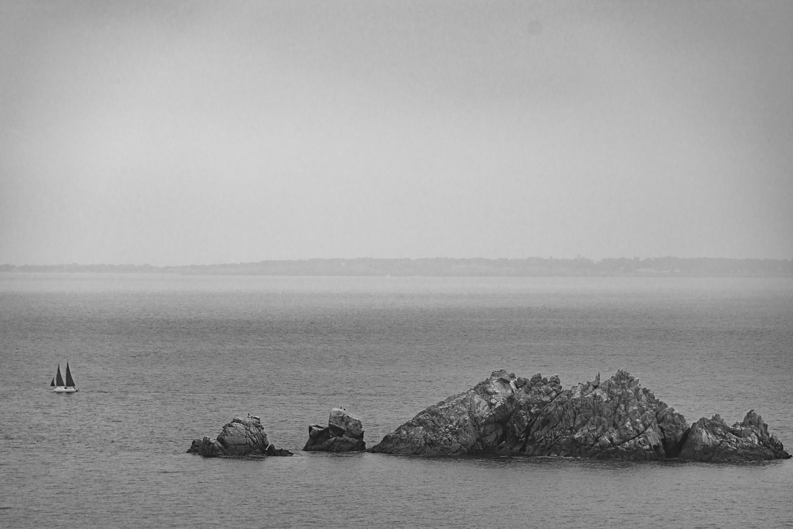 Einzelnes Segelboot segelt vor markanter Felseninsel, ruhiges Meer, vielfältige Farben, minimalistische Fotokunst in dokumentarischem Stil.