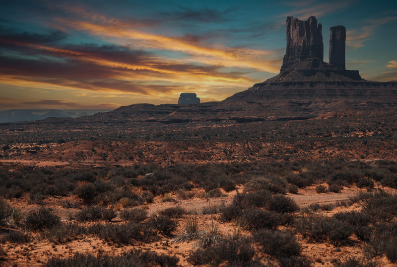 Monument Valley im Sonnenuntergang mit markanten Felsen, vielfältigen Farben und weitem Himmel, eingefangen in ruhiger, dramatischer Stimmung.